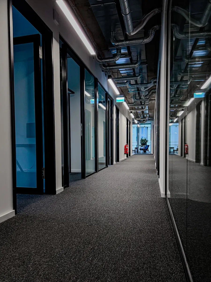 Modern office corridor with glass-walled offices and an open ceiling